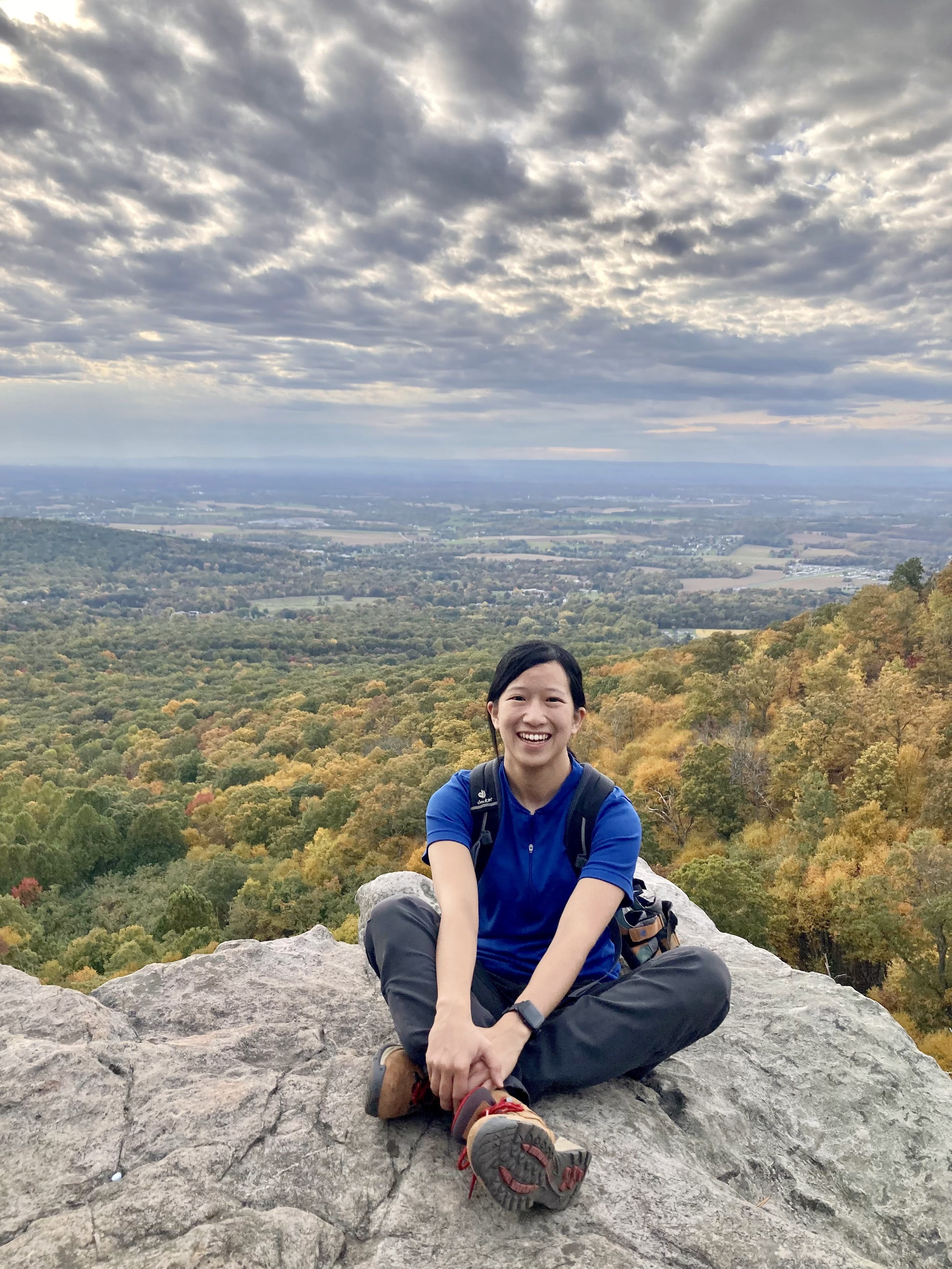 Stephanie Chia sitting on a rock overlooking a vally of yellow and green trees.