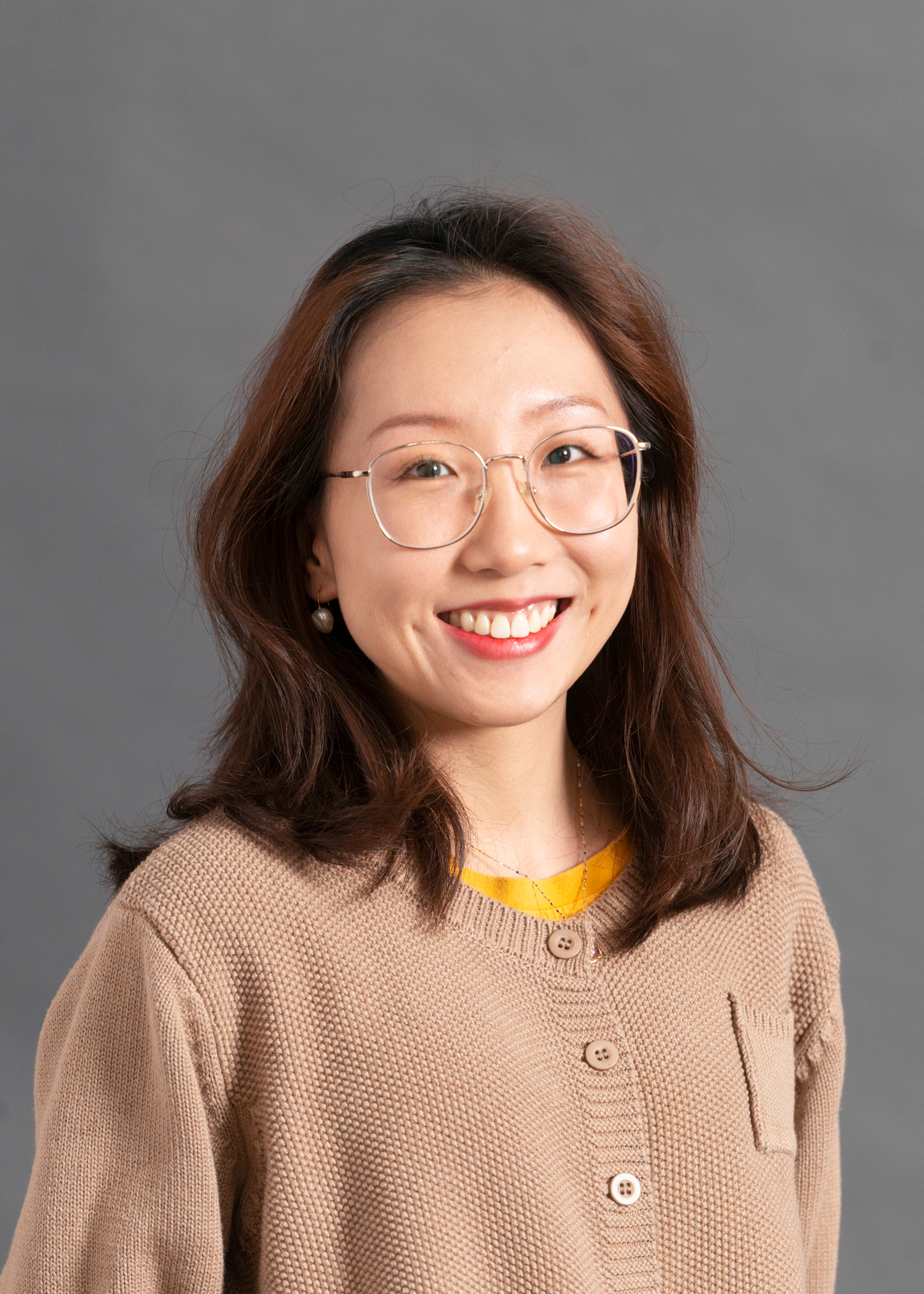 Jinyi "Cornelia" Zhu in a beige sweater and glasses smiles for a portrait.