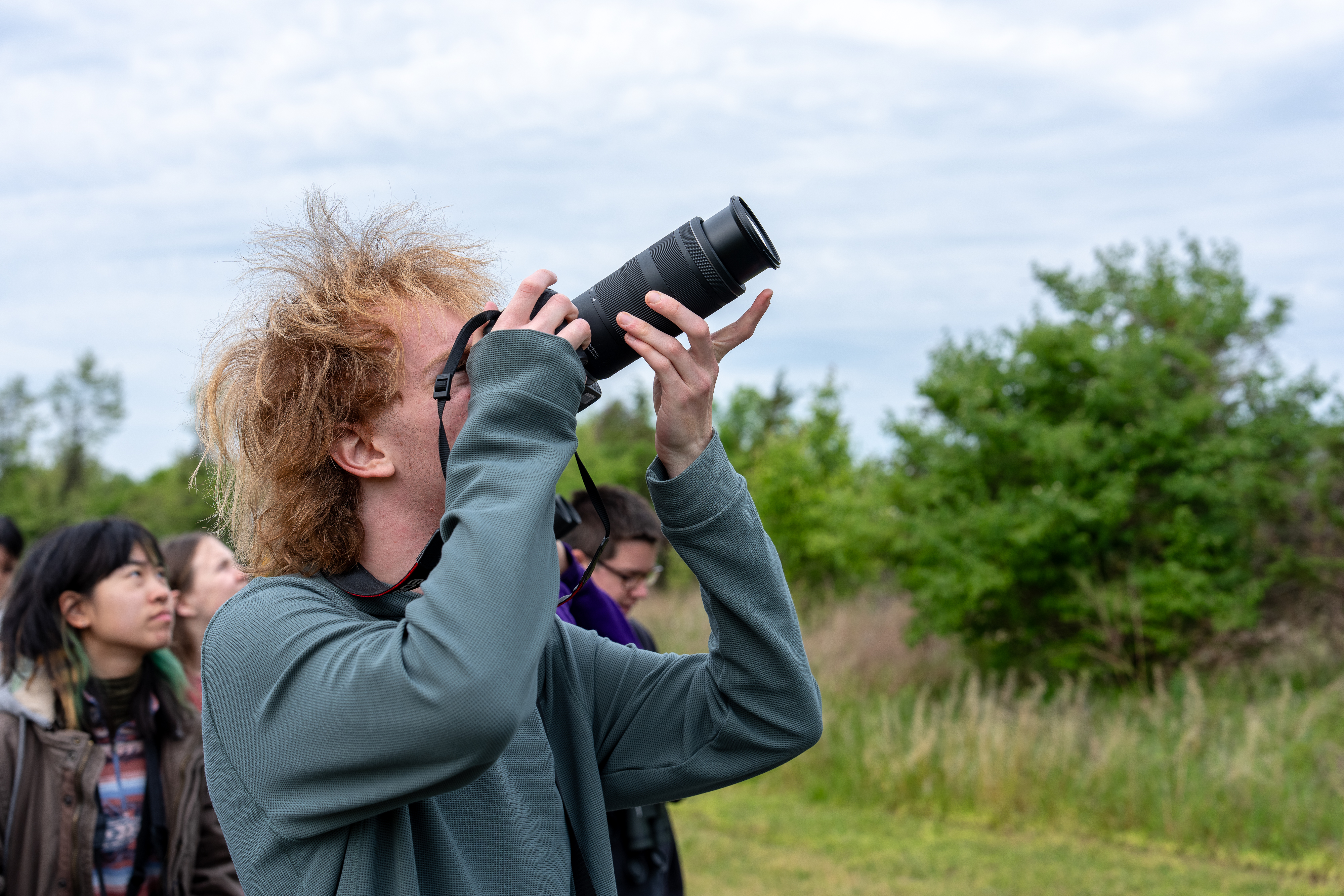 A red-headed man in a slate blue shirt looks toward the sky through a digital camera. 