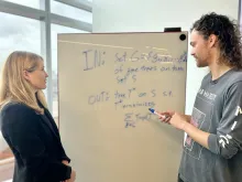 A woman, Dr. Erin Molloy, and a man (her student) are observing a whiteboard.