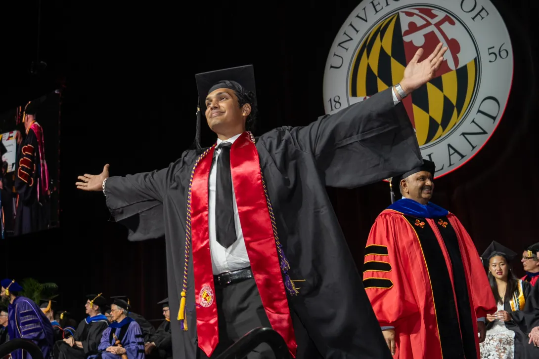 Graduate with arms raised after crossing the commencement stage